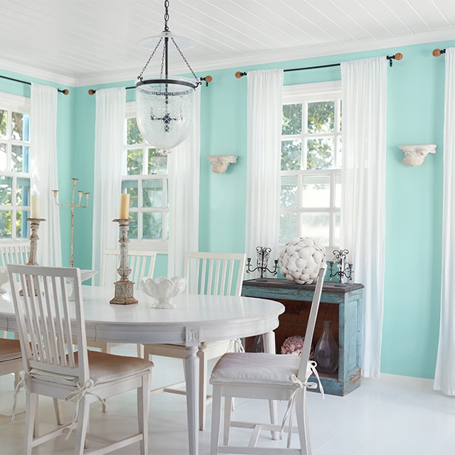 A pretty, light turquoise painted dining room with white trim, a white shiplap ceiling, and white dining furniture. A pretty, light turquoise painted dining room with white trim, a white shiplap ceiling, and white dining furniture.