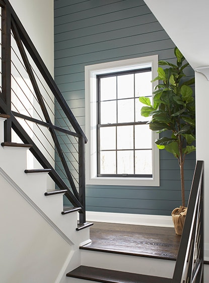 A wooden staircase with black metal handrail in a white room with a bluish gray accent wall.