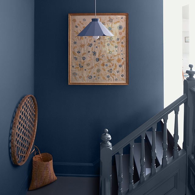 Dark blue painted corner walls with simple decor create a rich, monochromatic look next to a small light black painted staircase. Dark blue painted corner walls with simple decor create a rich, monochromatic look next to a small light black painted staircase.