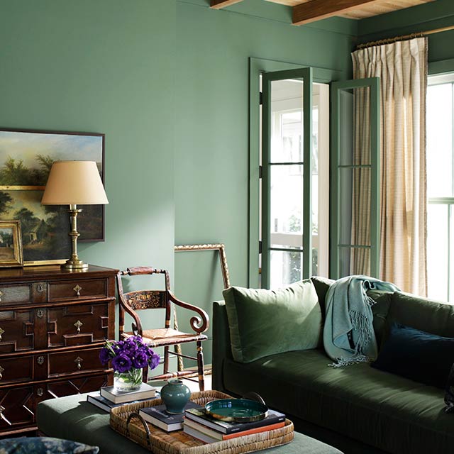 A green-painted English heritage style living room with green velvet sofas.