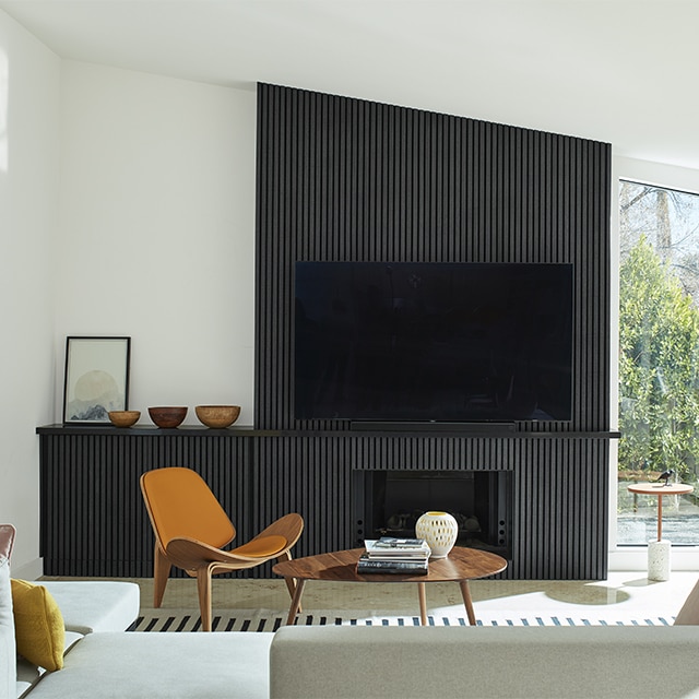 A mid-century modern style living room with bright, white-painted walls and vaulted ceiling, and a black paneled accent wall with a fireplace and large screen tv.