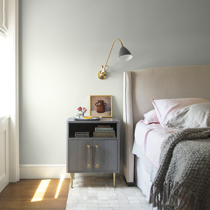 An airy bedroom with gray-painted walls and white trim features neutral bedding and metallic accents. Color of the Year 2019