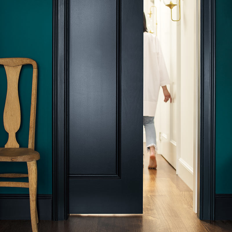 A deep blue-green-painted wall and navy-painted door opens to an off-white hallway. Color of the Year 2019
