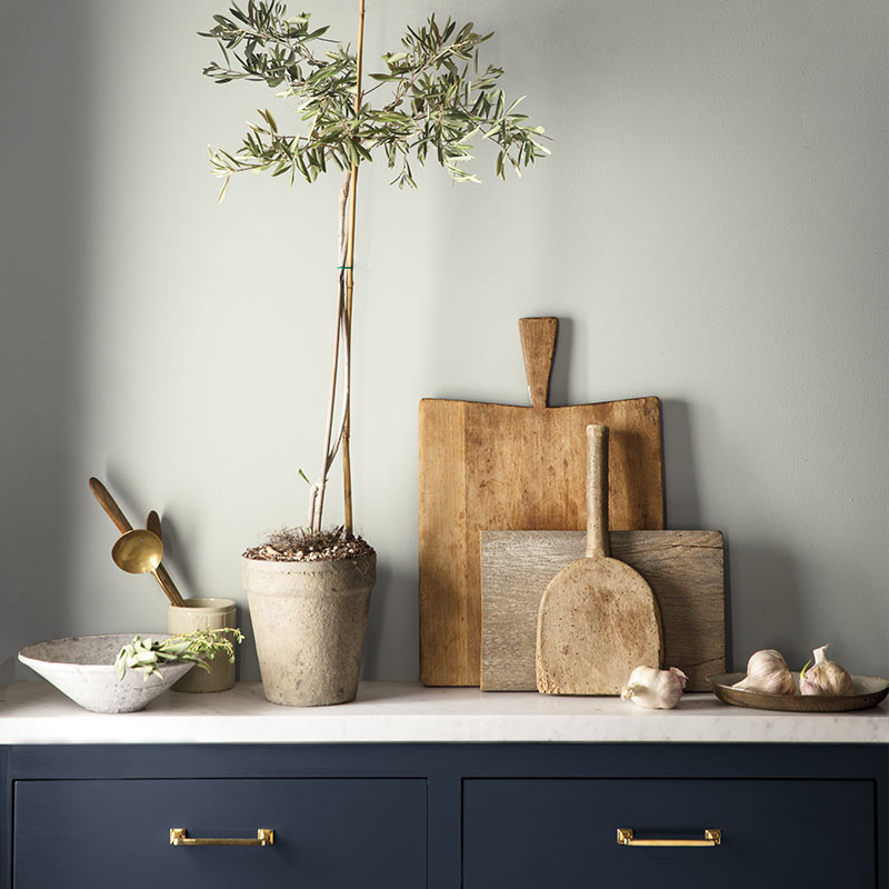 A navy-painted cabinet against a gray-painted wall features cutting boards and other kitchen items. Color of the Year 2019