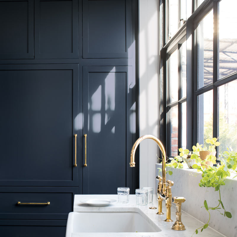 Navy-painted cabinets in a sleek kitchen with marble countertop, gold hardware and black trimmed windows. Color of the Year 2019