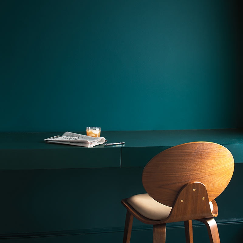 A rich teal wall with painted desk and armless wood chair. Color of the Year 2019