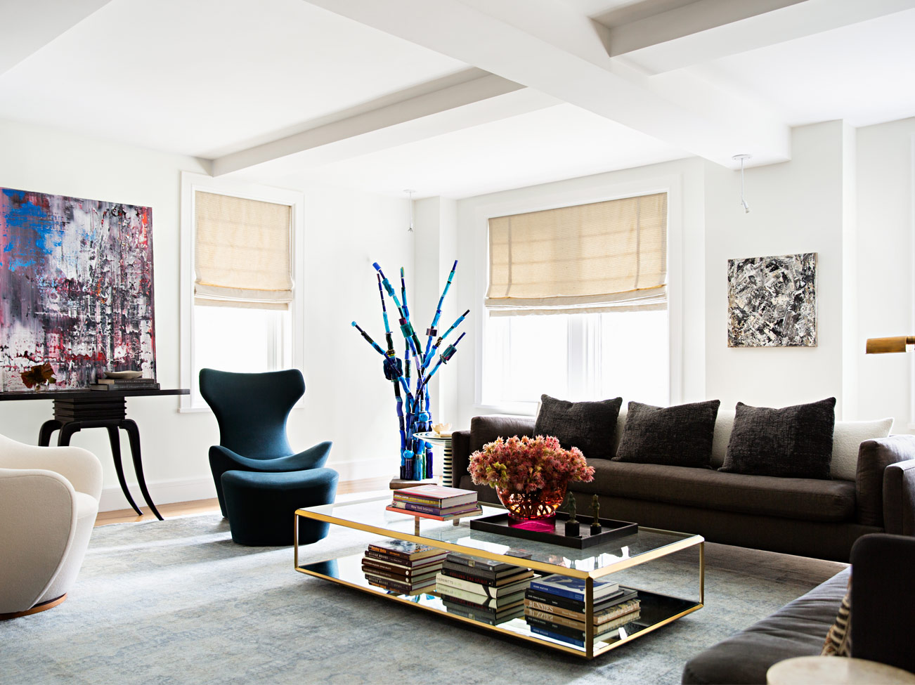 Salon blanc avec plafond à caissons, sofa brun, fauteuils modernes, table basse en verre au rebord doré et œuvres abstraites.