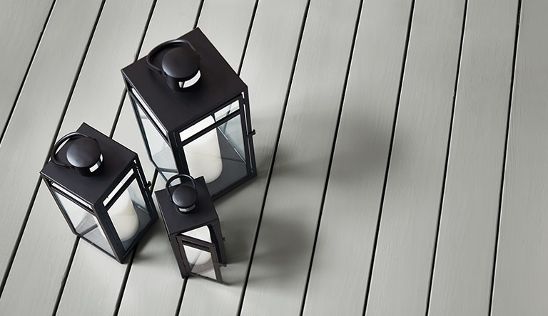Three black lanterns on a deck stained with Platinum Gray HC-179 Ultra Flat Solid Woodluxe® Exterior Stain.