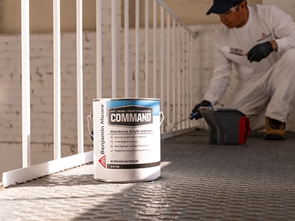 A gallon of Benjamin Moore Command® Waterborne Acrylic Urethane next to a painting contractor painting a white railing. A gallon of Benjamin Moore Command® Waterborne Acrylic Urethane next to a painting contractor painting a white railing.