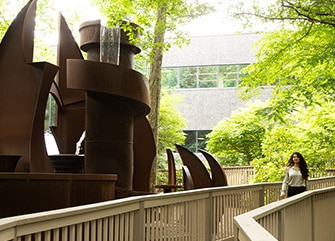An employee walks along the wooden pathway near a large modern sculpture, outside the Montvale office.