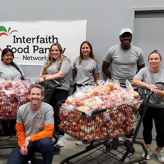 A group of Benjamin Moore employee volunteers pose with shopping carts filled with bagged apples.