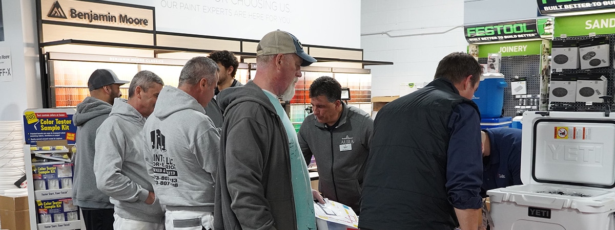 A group of painting contractors gathered near a red table with Benjamin Moore representatives at a Benjamin Moore store.
