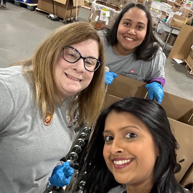 Three smiling employee volunteers in a warehouse.