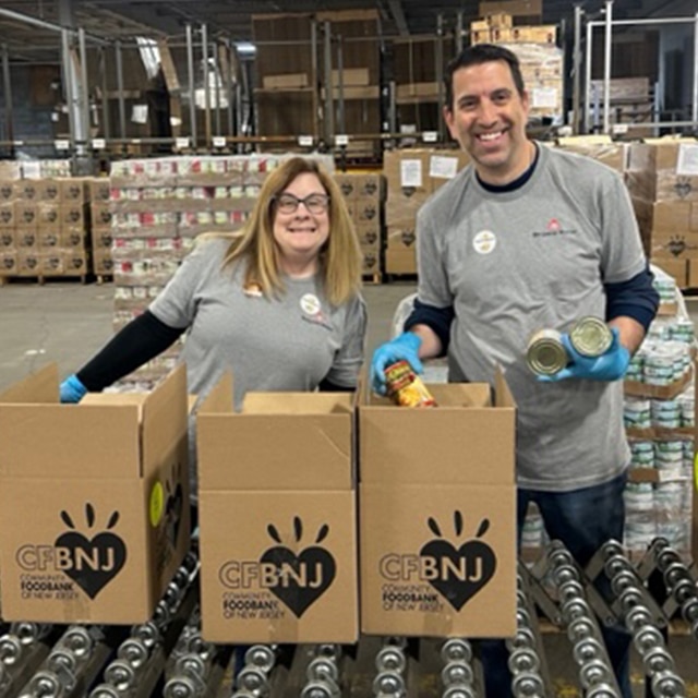 Two Benjamin Moore employee volunteers in a warehouse filling canned goods and food into cardboard boxes for a food bank.