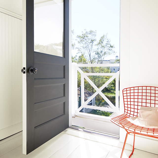 An entryway to a home with white-painted walls features an open black-painted door and a red, metal chair.