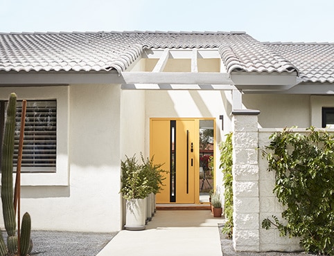 A white-painted stucco home exterior with a pretty yellow front door, a white tiled roof, and potted plants on the front walkway.