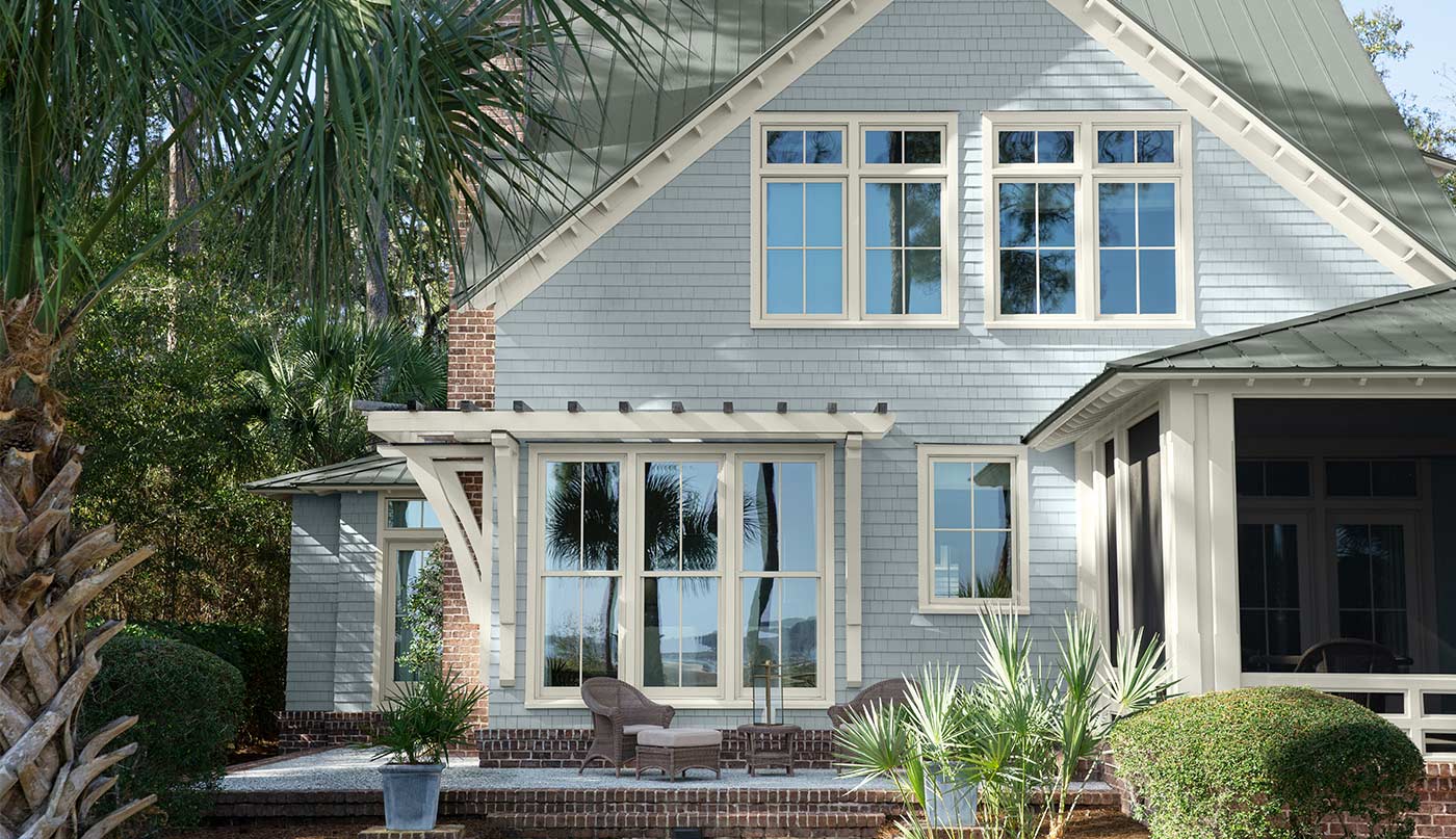A pretty light gray-painted home exterior with white garage doors and trim, a lush green lawn and landscaping.