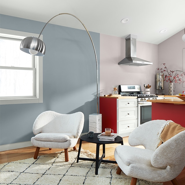 Un espacio de apartamento abierto y luminoso con una pared de la sala de estar pintada de azul claro, paredes de la cocina de color gris pálido con un toque de lavanda, un techo abovedado blanco, una isla de cocina de color rojo intenso, cajones de cocina blancos y una decoración moderna en blanco y negro.