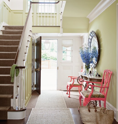 A front door opens into a pale green entryway featuring a console table and two colourful side chairs.