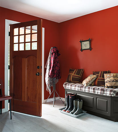 A deep red entryway does double duty as mud room with several pairs of boots lined up next to an upholstered bench.