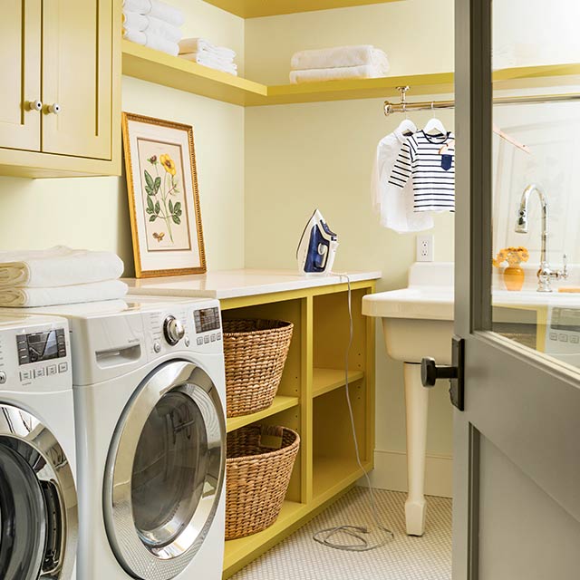 A cream laundry room with built-in shelves and cabinets in a midtone yellow colour.