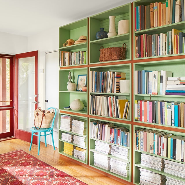 Vestibule accueillant avec bibliothèque pleine longueur verte, plafond et murs blancs, cadre de porte d’entrée rouge et petit tapis rouge.