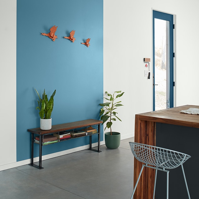 A contemporary white-painted entryway with a blue-trimmed door, and a rich blue-painted rectangle graphic behind a wooden bench, and a wood and charcoal gray-painted island with mesh bar stool.