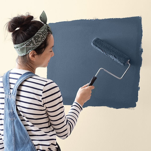 A woman rolling dark blue paint onto a wall.