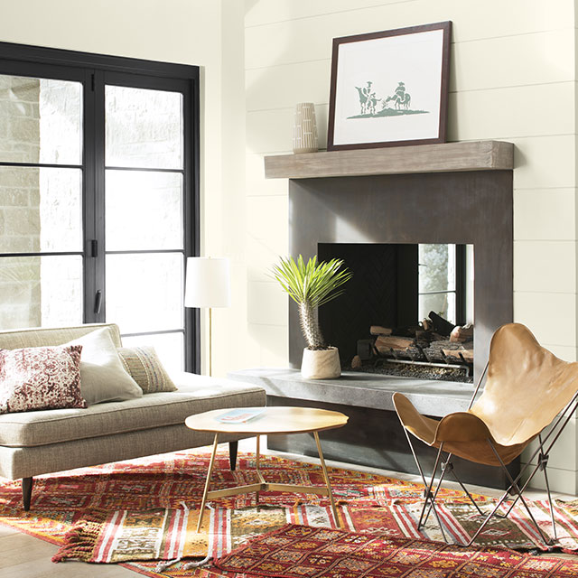 Un salon peint en blanc arborant un foyer en pierre grise, un canapé gris, une chaise d’accent brune et une table en bois.