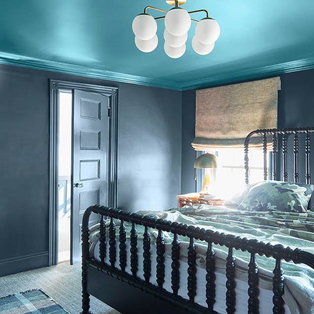 Habitación con paredes, marcos y puerta pintados de azul grisáceo oscuro, techo en azul brillante y cama con barrotes negra.