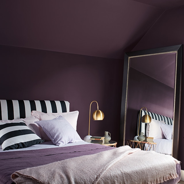 Habitación pintada de Morado Oscuro con marco blanco, un cabezal y una almohada a rayas blancas y negras, y mantas púrpuras y blancas.