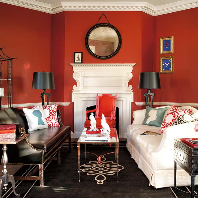 Sala de estar pintada de rojo con repisa de chimenea, techo y marco en blanco; un sofá blanco y uno negro, decoración clásica y piso decorativo oscuro.