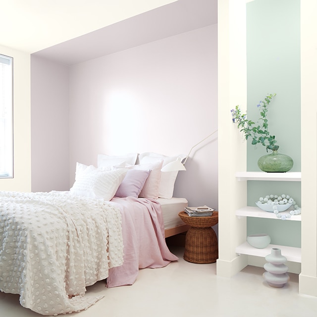 A white bedroom with violet inset and a blue-green accent behind white shelving, bed with white and violet bedding.