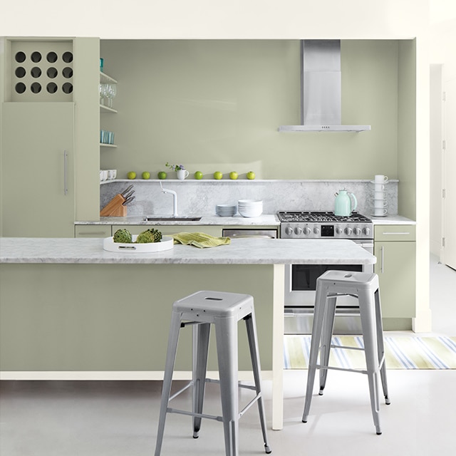 A sage green-painted kitchen with bar seating, silver appliances, and a variety of kitchen utensils.