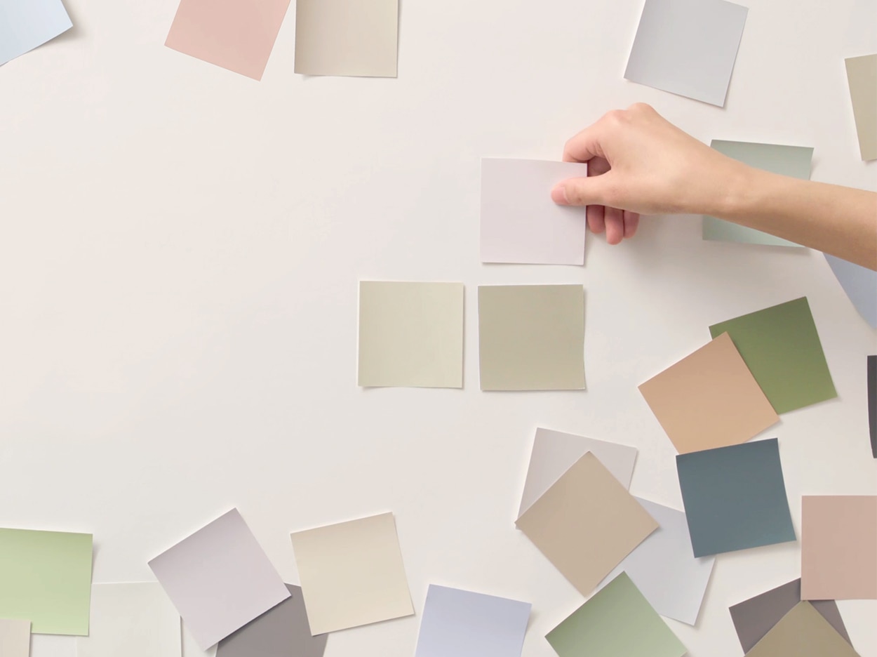 A person applying various color swatches on a white wall.