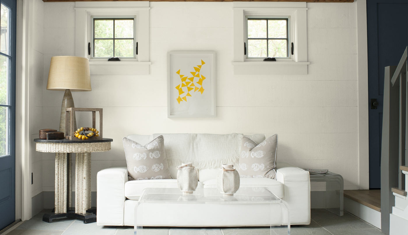 A bright sitting room with white shiplap walls accented by neutral fabric furniture and accessories.