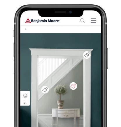 A smart phone with the Benjamin Moore Color Portfolio app showing a dark gray wall with white trim, looking into a light gray hallway with white trim, a white table and green topiary.