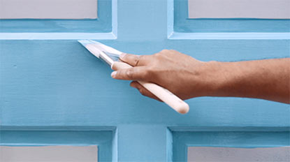 A person brushing blue paint onto a door.