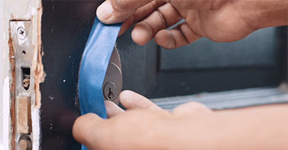 A person applying painter’s tape around a door deadbolt.