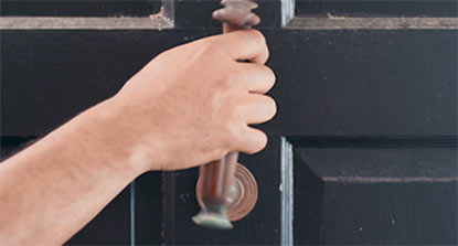 A person removing hardware from an exterior door in preparation for painting.  