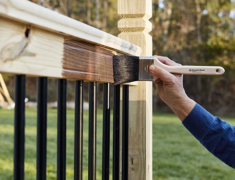 A person brushing stain onto a wood railing.