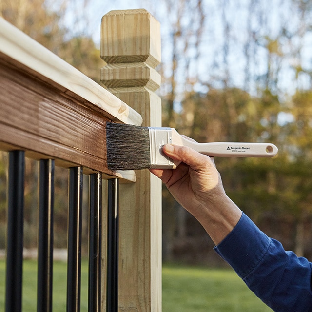 A person brushing stain onto a deck railing.
