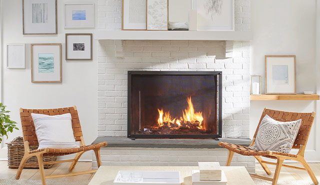 A white wall with framed artwork and white-painted brick fireplace flanked by matching leather and wood chairs.