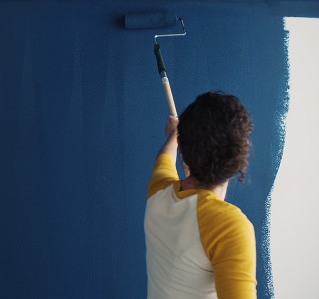 Un propriétaire applique au rouleau la couleur Bleu Symphonie 2060-10 sur un mur.