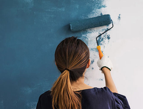 Mujer pintando una pared de azul con rodillo.