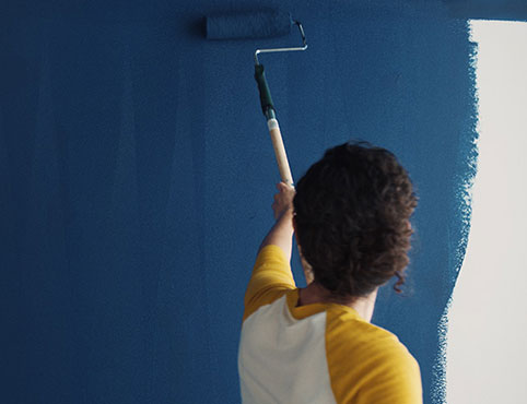 A homeowner uses a roller to paint Symphony Blue 2060-10 on a wall.