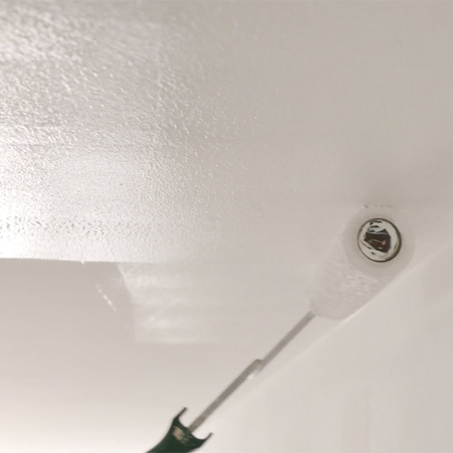 A closeup of white paint being rolled onto a ceiling.