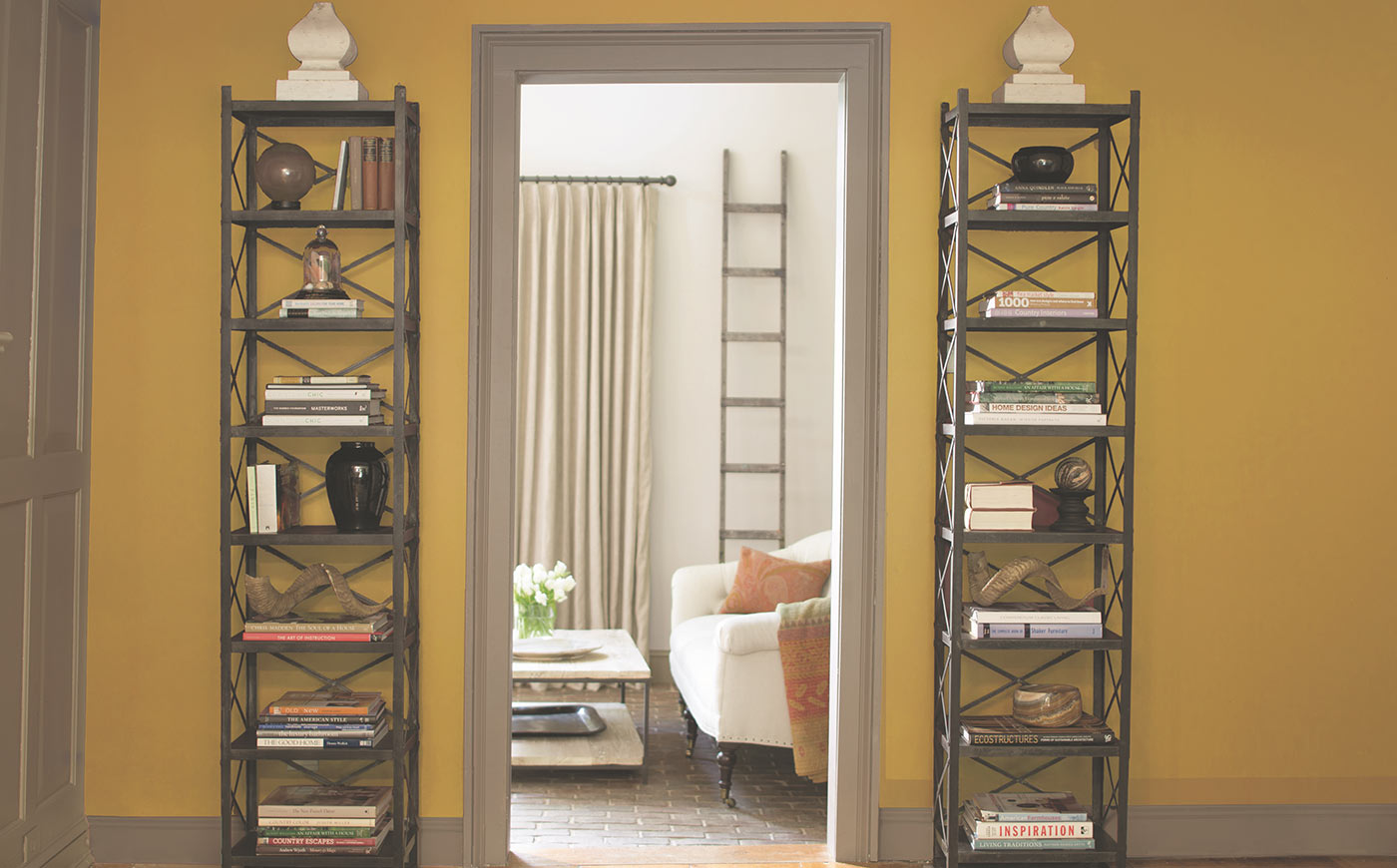 Paredes de color amarillo y pasillo con un marco gris que conduce a una acogedora sala de estar pintada de blanco.