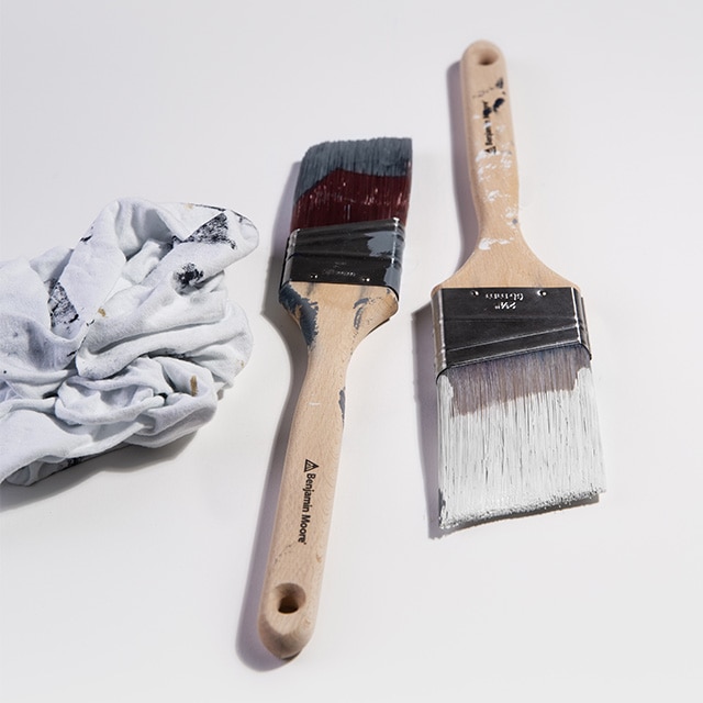 Two Benjamin Moore paintbrushes: one with white paint on it and the other with black paint, next to a white cloth.