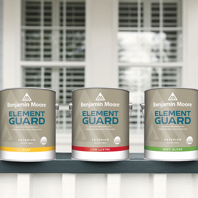 Tres galones de Element Guard® Pintura para exteriores cerca de las barandillas de un porche azul y blanco, delante de una ventana.